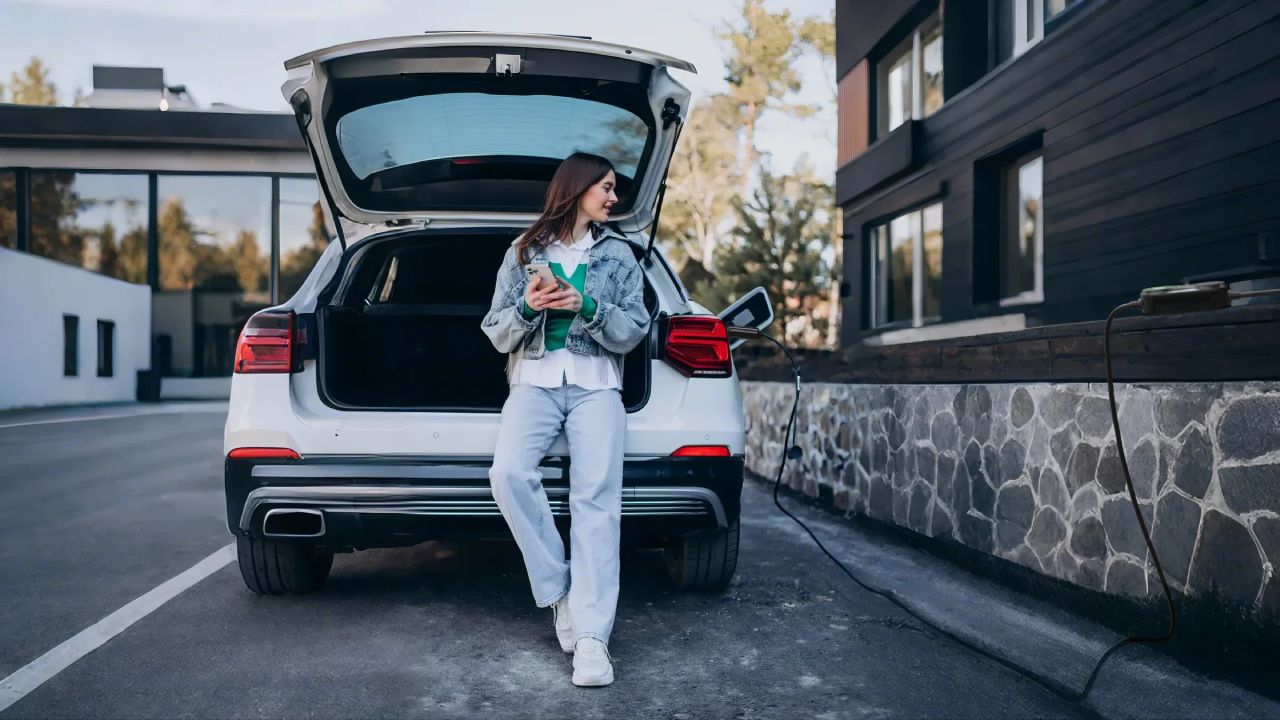 Woman leaning on an electric vehicle while charging with a Type 2 EV portable charger outside a modern house