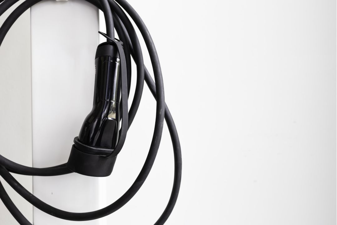 Close-up of an EV charging cable hanging on a wall-mounted charging station, showcasing sleek design and durability.